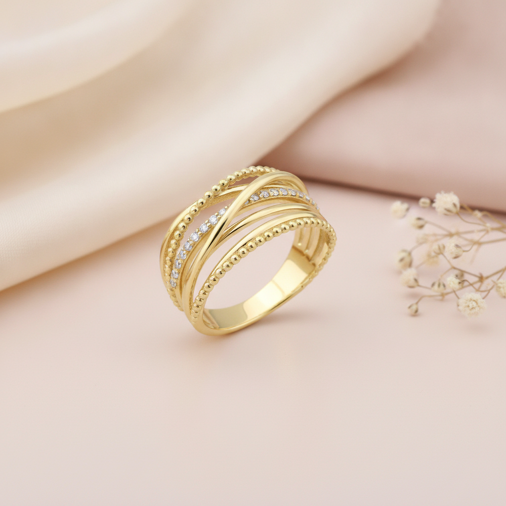 intertwined gold ring with beaded strands and White CZ stones on a blush background with draped satin fabric and baby's breath