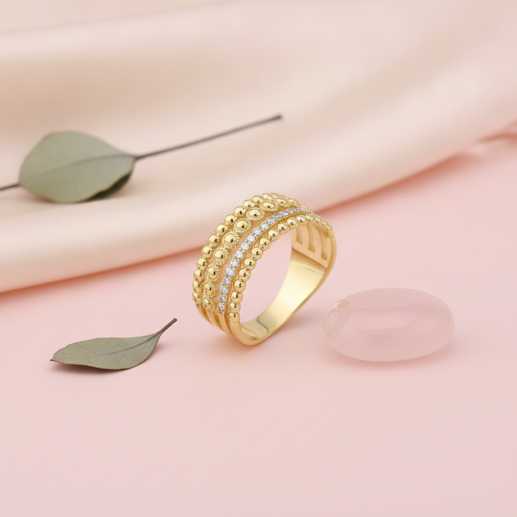 wide gold beaded ring with a row of White CZ stones on a blush background with draped satin fabric and a rose quartz stone