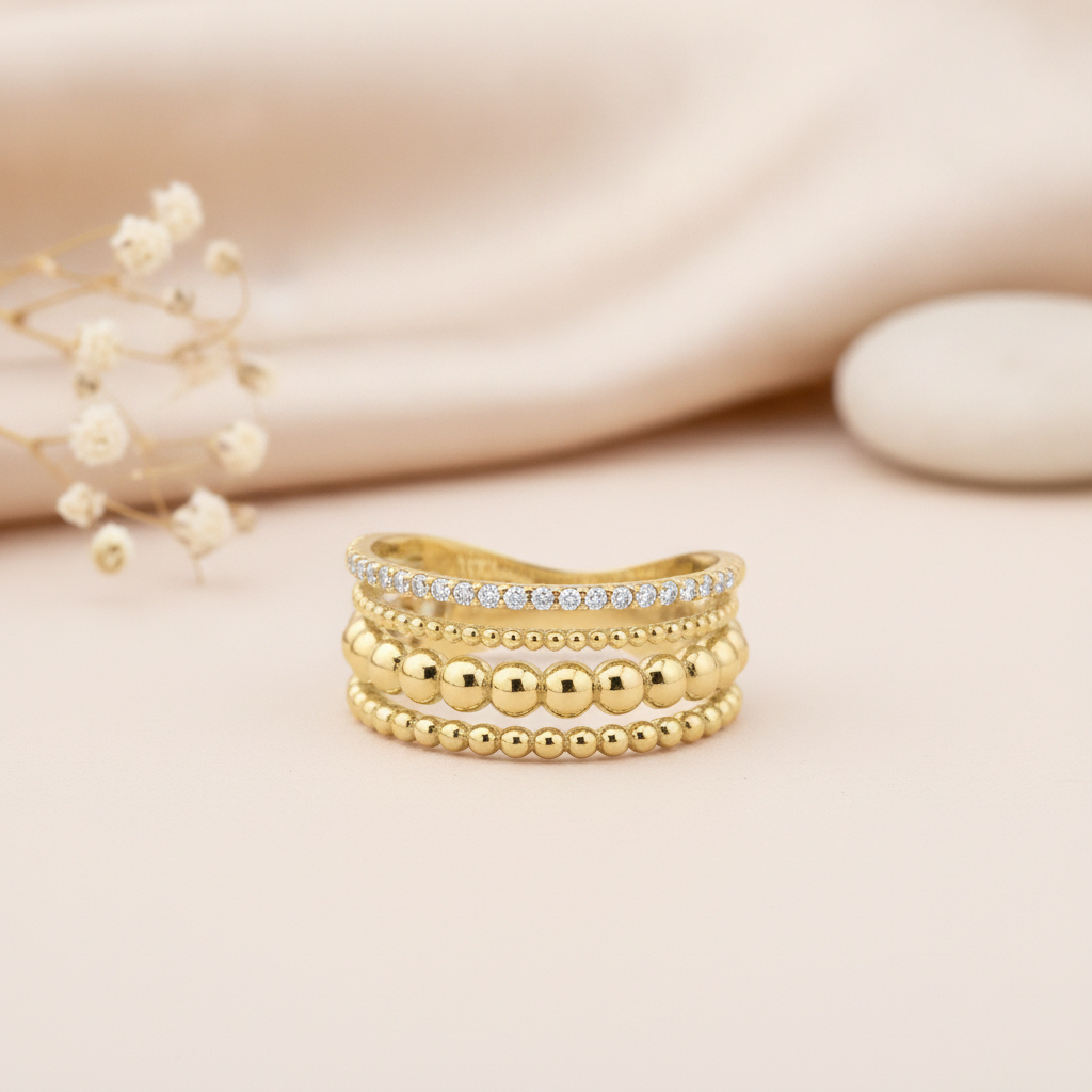 multi-row gold stack ring with beaded texture and White CZ stones on a pink background with a eucalyptus leaf and a rose quartz stone