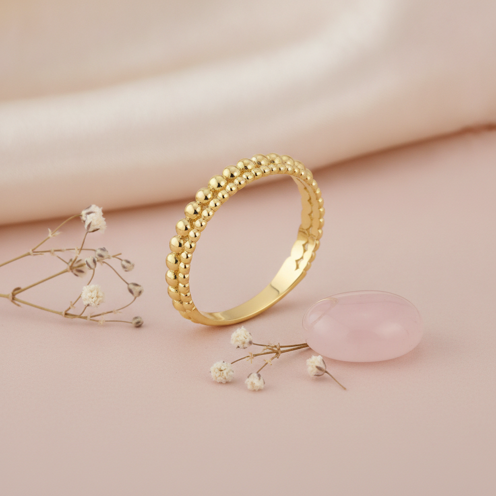 double row gold beaded ring with larger and smaller spheres on a blush background with dried baby's breath and a rose quartz stone