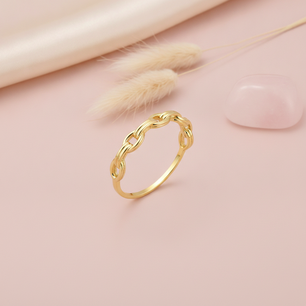 gold interlocking chain-link ring on a blush background with dried pampas grass and a pink stone