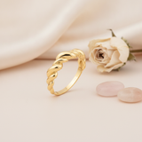 twisted gold ridged band ring on a cream background with draped satin fabric and a dried rose with rose quartz stones
