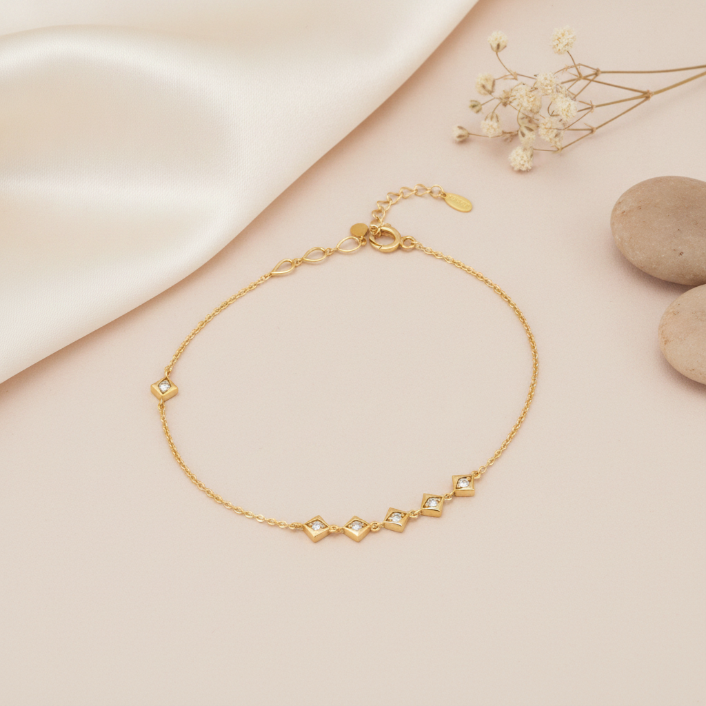 gold chain bracelet with four square White CZ stone stations and a single accent stone on a blush background with baby's breath and stones