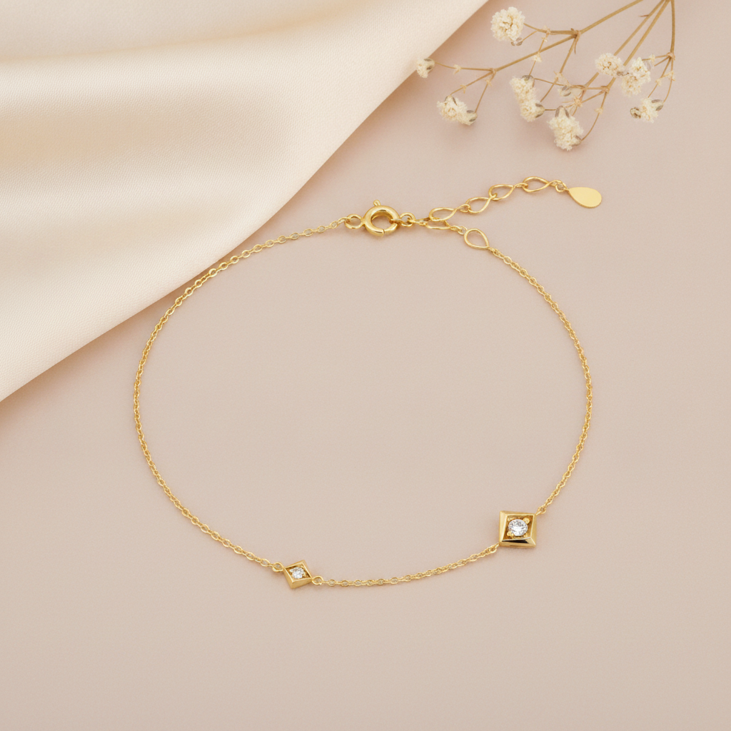 gold chain bracelet with two square White CZ stone settings on a blush background with an adjustable clasp visible and baby's breath