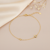 gold chain bracelet with two square White CZ stone settings on a blush background with an adjustable clasp visible and baby's breath