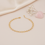 gold linked kite frame bracelet with stones on a blush background with draped satin fabric and a rose quartz heart