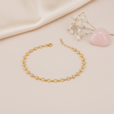 gold linked kite frame bracelet with stones on a blush background with draped satin fabric and a rose quartz heart