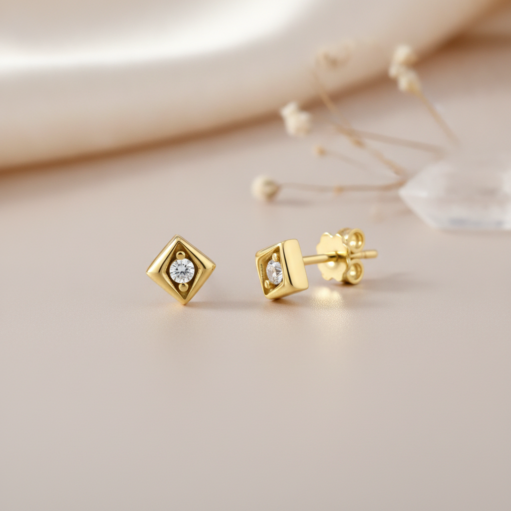gold geometric stud earrings with a recessed White CZ stone on a cream background with a dried flower sprig