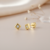 gold geometric stud earrings with a recessed White CZ stone on a cream background with a dried flower sprig