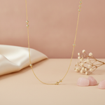 gold chain necklace with clustered kite-shaped stone stations on a mauve background with draped satin fabric, baby's breath, and rose quartz stones