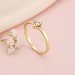 slender gold ring with a single White CZ stone in a square bezel on a pink background with dried baby's breath