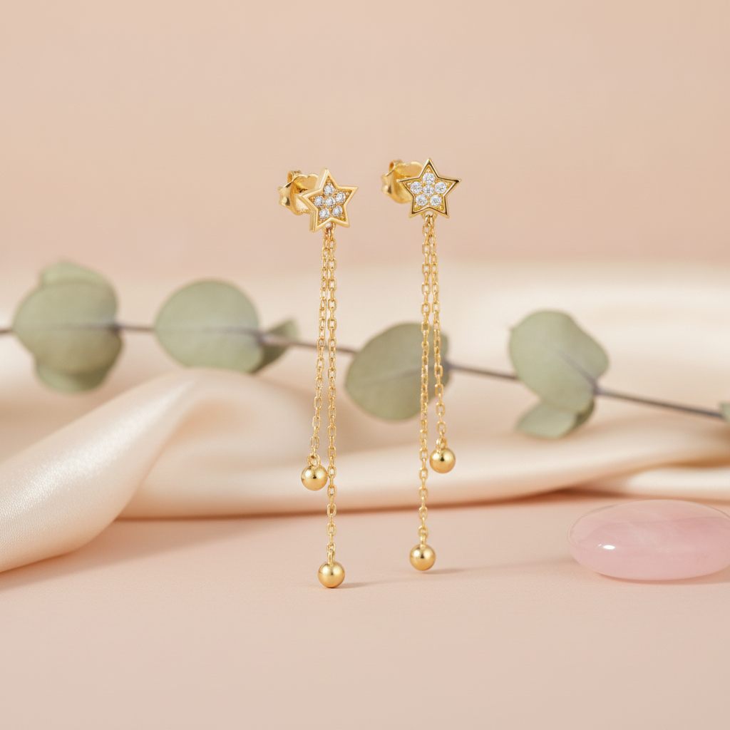 gold star stud earrings with cascading chains and polished spheres on a blush pink backdrop with eucalyptus leaves and a rose quartz stone