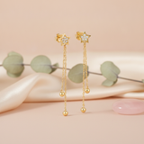 gold star stud earrings with cascading chains and polished spheres on a blush pink backdrop with eucalyptus leaves and a rose quartz stone
