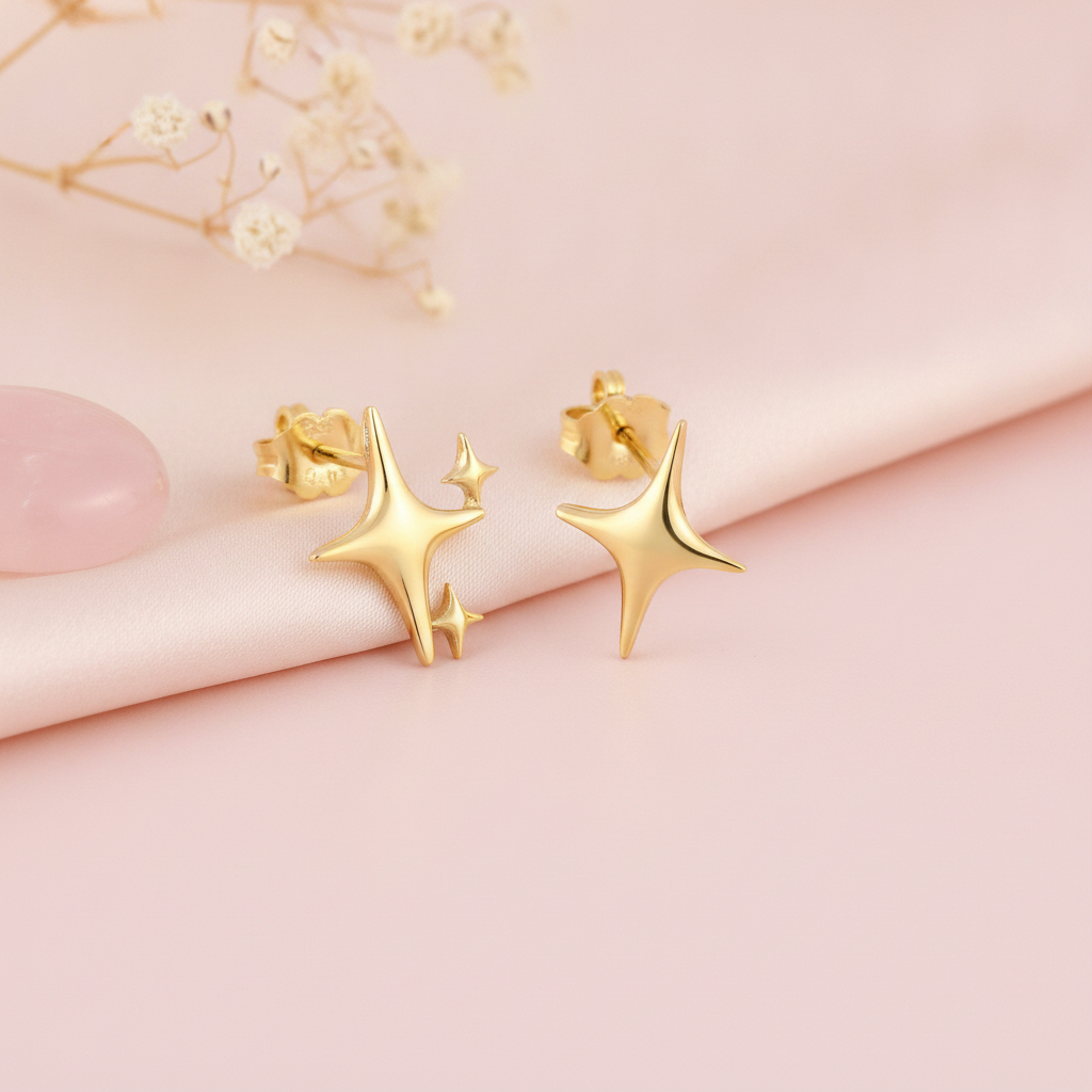 sculpted gold star stud earrings with one large star and two small accent stars on a pink backdrop with dried baby's breath and a rose quartz stone