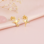 sculpted gold star stud earrings with one large star and two small accent stars on a pink backdrop with dried baby's breath and a rose quartz stone
