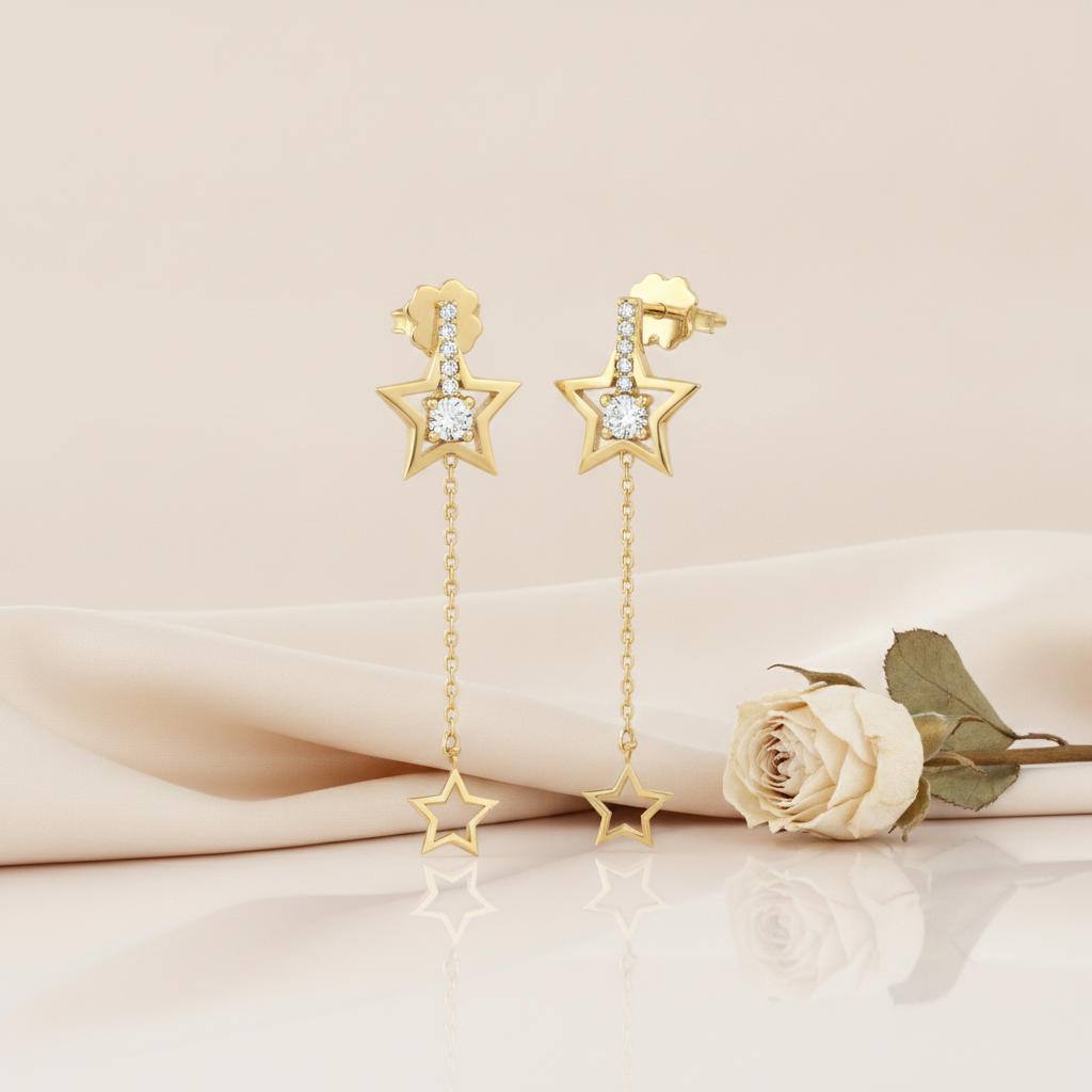 gold drop earrings with a stone-set open star and a dangling star outline charm on a blush backdrop with a dried cream rose