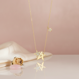 gold star pendant necklace with an interlocking paved star and a dangling star charm on a pink backdrop with a dried rose and a pink stone