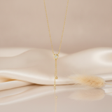 gold star pendant necklace with an asymmetrical dangling chain and a gold sphere on a blush backdrop with dried grass