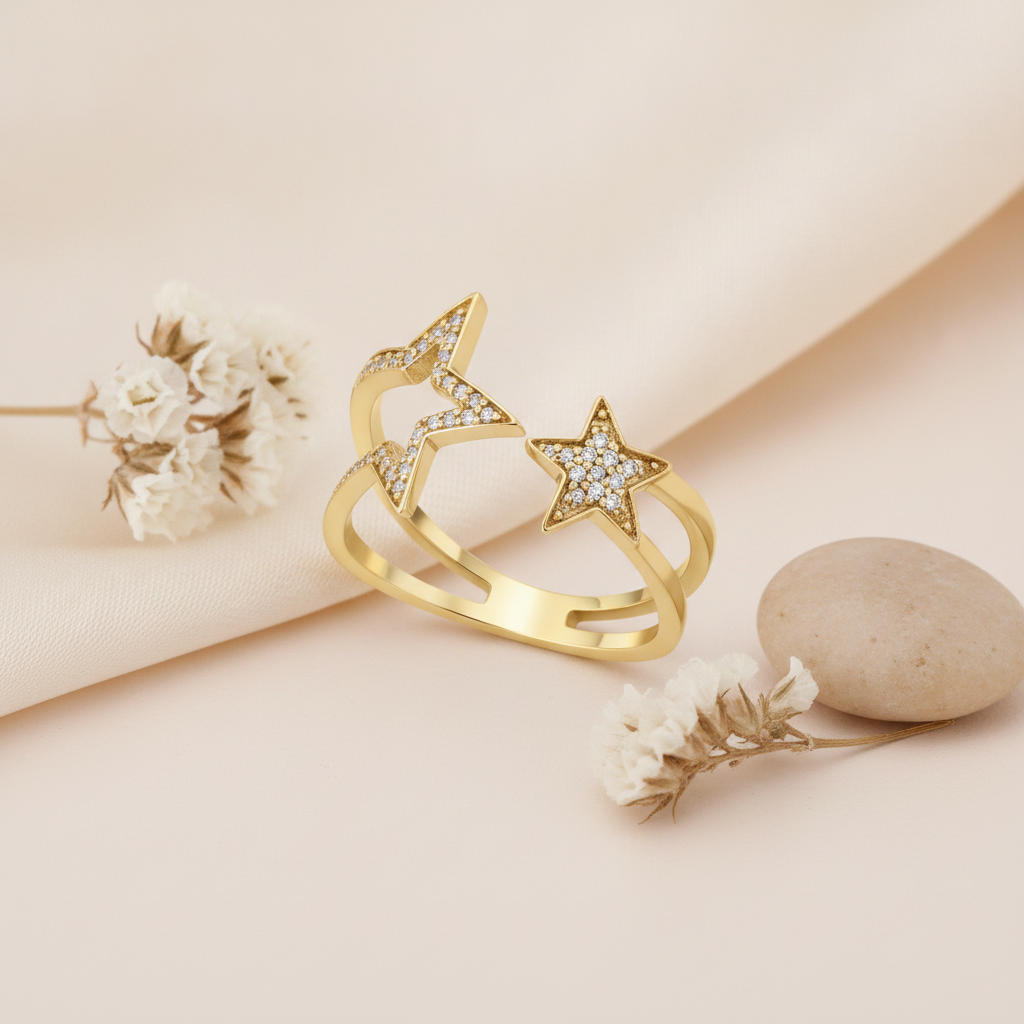 gold double-band ring with a large outlined star and a smaller star on a blush pink backdrop with dried flowers