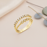 gold double-band ring with a row of clear stones and three beaded star motifs on a blush backdrop with dried flowers and a stone