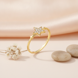 gold ring with a stone-set four-pointed star and smaller star accents on a pink backdrop with dried flowers