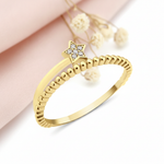 gold ring with a beaded band and a stone-set star on a blush backdrop with a soft feather and a stone