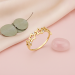 gold ring with a row of openwork stars and round stones on a pink backdrop with dried flowers