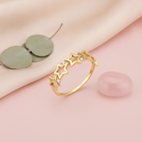 gold ring with a row of openwork stars and round stones on a pink backdrop with dried flowers