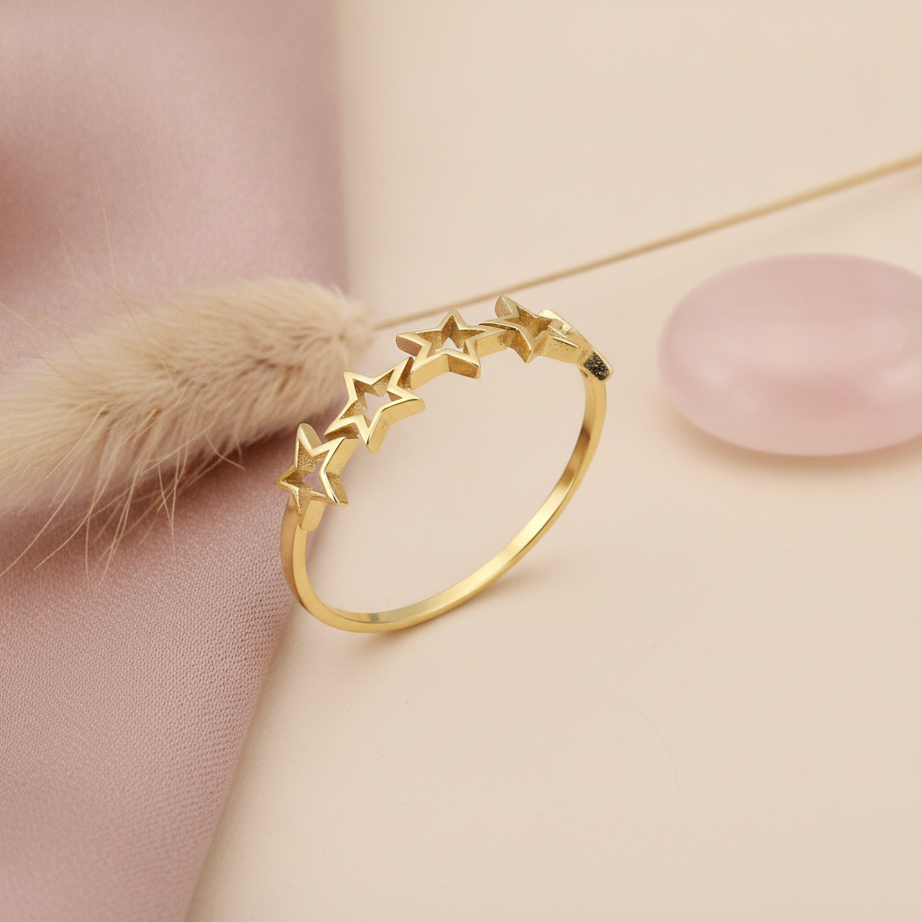 polished gold ring with five interconnected openwork star silhouettes on a blush backdrop with dried flowers and a rose quartz stone