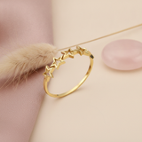 polished gold ring with five interconnected openwork star silhouettes on a blush backdrop with dried flowers and a rose quartz stone