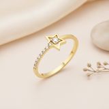 gold open ring with a star frame, a center stone, and a cascading row of stones on a pink backdrop with dried seed pods