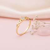 gold ring with a stone-set central star and a sequence of open star silhouettes on a blush backdrop with dried flowers and a rose quartz stone