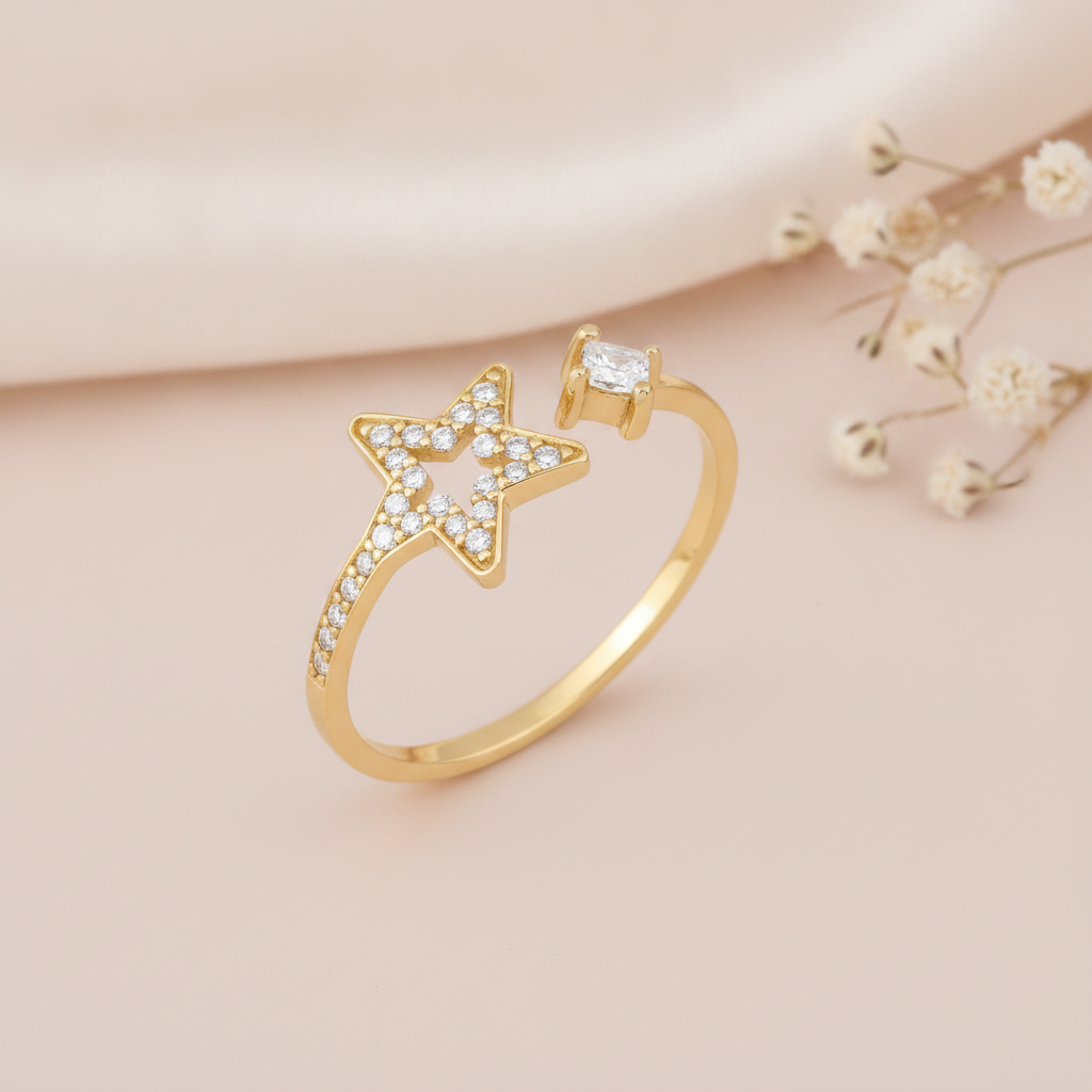 gold open bypass ring with a stone-set star outline and a princess-cut stone on a pink backdrop with dried baby's breath