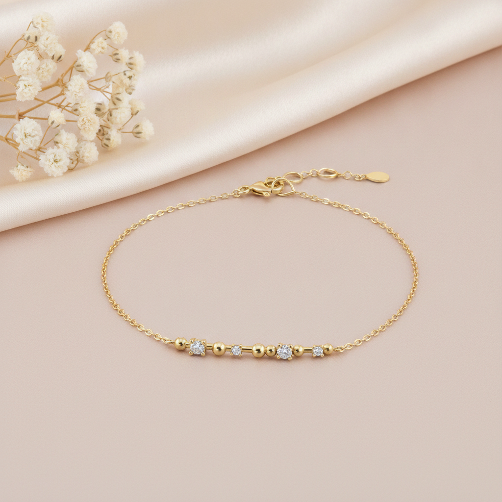 gold chain bracelet with a beaded and stone-set bar station on a pink backdrop with dried baby's breath