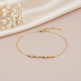 gold chain bracelet with a beaded and stone-set bar station on a pink backdrop with dried baby's breath