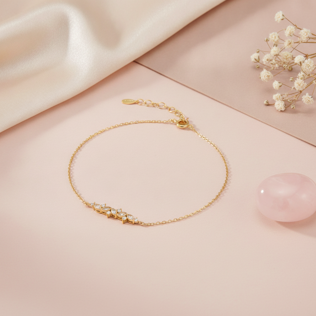 gold chain bracelet with a curved cluster of marquise and round stones on a pink backdrop with a logo tag charm, dried flowers, and a rose quartz stone