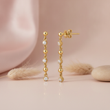 gold linear drop earrings with alternating stones and gold spheres on a blush backdrop with a feather and a stone