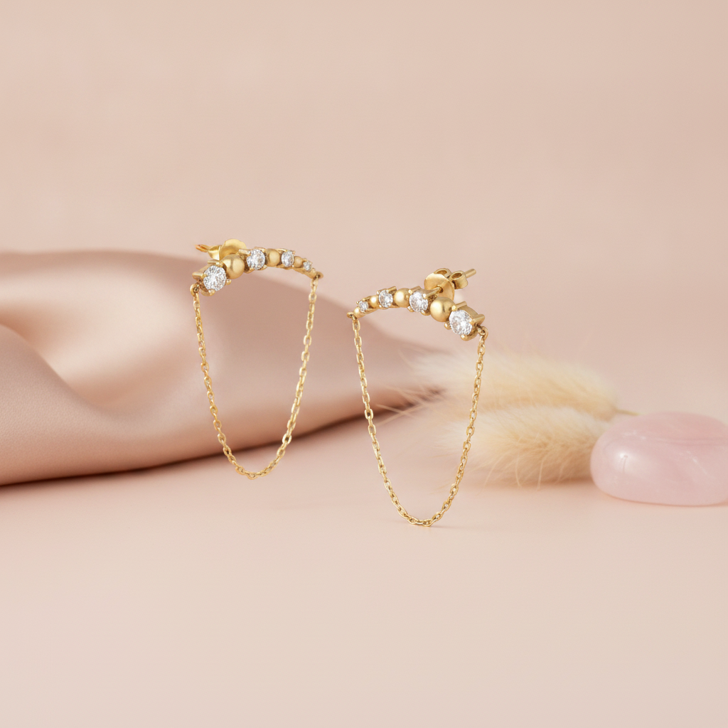 gold bar earrings with spheres, stones, and a softly draped chain on a pink backdrop with dried flowers and a rose quartz stone
