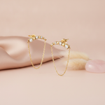 gold bar earrings with spheres, stones, and a softly draped chain on a pink backdrop with dried flowers and a rose quartz stone