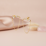 gold bar earrings with spheres, stones, and a softly draped chain on a pink backdrop with dried flowers and a rose quartz stone