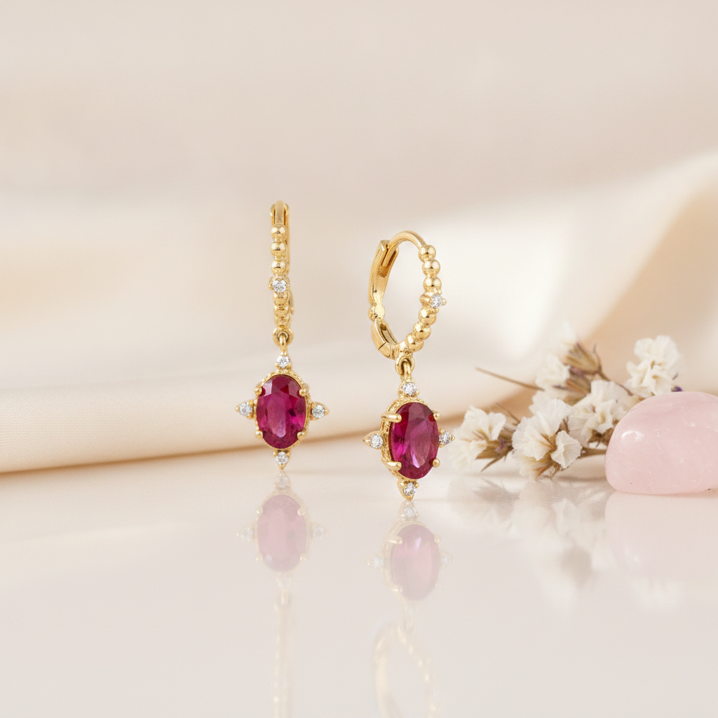 gold huggie hoop earrings with a dangling oval red gemstone on a cream backdrop with dried flowers and a rose quartz stone