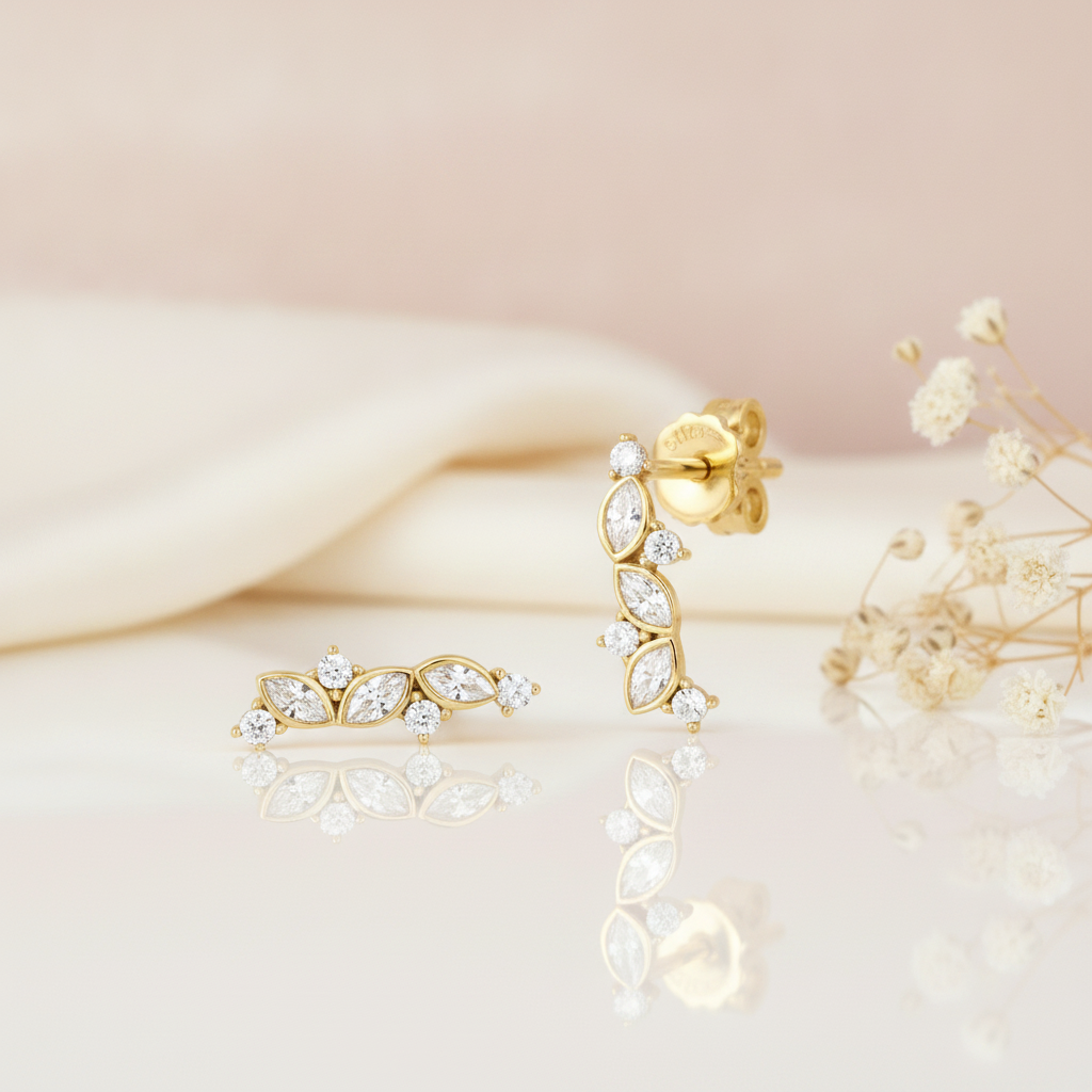 gold ear climber earrings with three marquise-cut stones on a pink backdrop with dried flowers