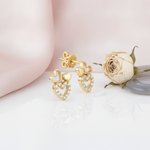 gold heart stud earrings with a solid heart, an open heart, and a pave-set heart on a pink backdrop with a dried rose and a stone