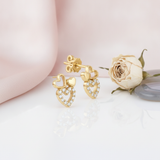 gold heart stud earrings with a solid heart, an open heart, and a pave-set heart on a pink backdrop with a dried rose and a stone