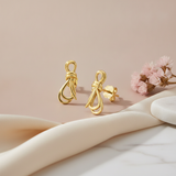 gold knot stud earrings with interlocking loops on a pink backdrop with dried pink flowers and a marble surface