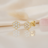 gold flower cluster stud earrings with round stones on a cream backdrop with a dried grass stem and a rose quartz stone