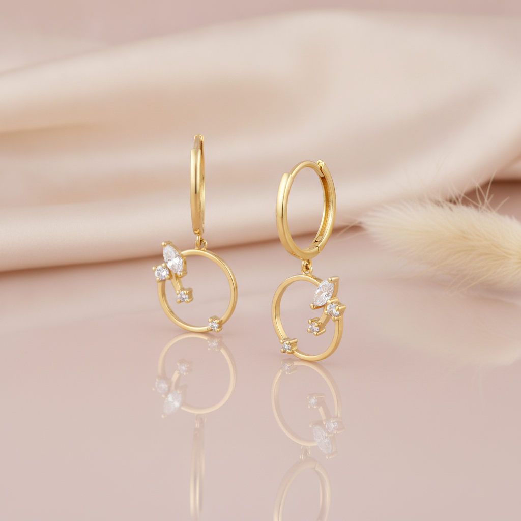 gold huggie hoop earrings with a suspended open ring and a stone cluster on a pink backdrop with dried grass