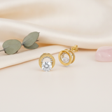 gold circle stud earrings with a round center stone and a pave-set halo on a cream backdrop with eucalyptus leaves and a rose quartz stone