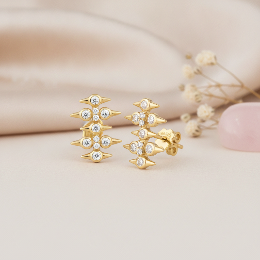 gold spike stud earrings with round stones on a cream backdrop with dried flowers and a rose quartz stone
