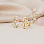 gold spike stud earrings with round stones on a cream backdrop with dried flowers and a rose quartz stone